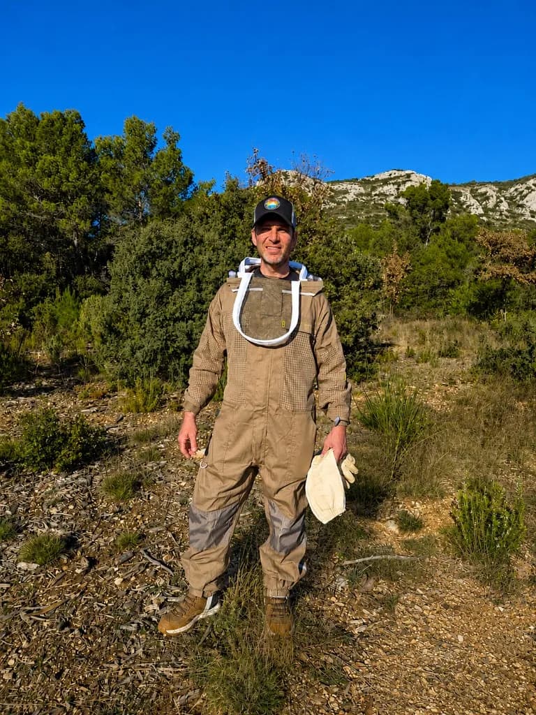 Sébastien Richet, apiculteur des Ruchers des Richet, en tenue de protection devant les collines de Jouques en Provence